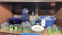 Shelf with blue ceramic bowl, cobalt plates, blue decanter, juice glasses and napkin rings