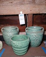 Front view of three green pottery jardinieres showing size and designs