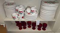 Stacks of plates and mugs with floral bird motif alongside ruby goblets