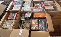 Open moving boxes showing many jigsaw puzzle boxes of various brands and sizes