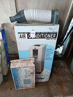 Toyotomi TID-1800 air conditioner box with vent hose on top and boxed winter cover leaning against it