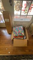 Closed cardboard shipping box and open box containing stacked wrapping sheets; boxed tree stand visible