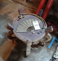 Top view showing folded metal fan with phoenix motif on round carved stand
