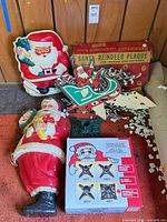 Lot overview showing blow-mold Santa, flat Santa plaque, boxed plaque set, tree stand and stakes