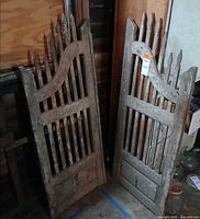 Two weathered wooden saloon-style gates leaning against wall