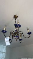 Chandelier hanging from ceiling, showing brass arms, cobalt porcelain bobeches and floral center finial