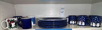 Dinner plates stacked with surrounding mugs on shelf