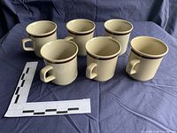 Six tan stoneware mugs grouped upright