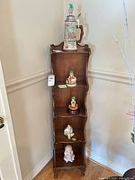Tall display shelf showing beer stein on top and multiple Hummel figurines on lower shelves