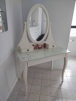 Front view showing entire white wood vanity, oval mirror, two small box drawers, glass top and cabriole legs