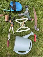 All nine garden items laid out on grass for overview: watering can, two sprinklers, bulb planter, hedge shears, pruners, cultivator, hose nozzle, kneeling pad