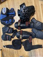 All martial arts protective items arranged on floor showing both headguards, shin guards, gloves, foot guards and elbow pads