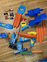 Overview of assorted Hot Wheels orange track sections, blue ramps, launchers, connectors and eight die-cast cars