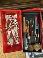 Open red plastic art box showing paint tubes, brushes, palette knife, sponges