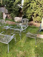 Glass-top patio table with four cast aluminum chairs on lawn