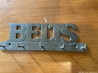 Front view of cast brass belt hanger showing lettering, hooks and mounting holes