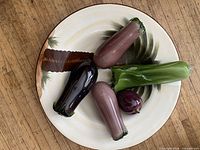 Four elongated glass vegetables and one small round glass vegetable displayed on a plate (plate excluded)