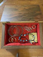 open jewellery box showing bangles, earrings, ring, necklaces inside red felt interior
