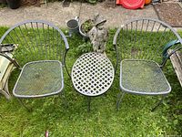Front view of two metal patio chairs and round metal side table on lawn