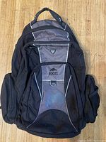 Front view showing Roots logo, grey accent, reflective piping, zip compartments