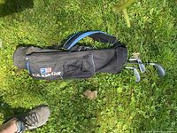 Full view of U.S. Kids Golf junior carry bag lying on grass with three clubs inside