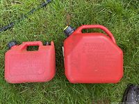 Two red plastic gasoline cans on grass