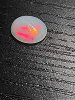 Oval cabochon Ethiopian fire opal on textured black surface, showing red and orange fire