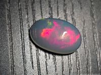Oval jelly opal cabochon with bright pink and green play-of-colour on textured black background
