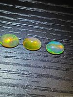 Three oval cabochon opals on dark surface, showing size and colour
