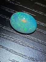 Oval Ethiopian opal cabochon on textured surface, showing play-of-color