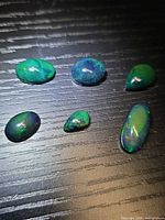 Six black opal cabochons on dark surface