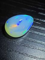 Pear cabochon opal showing play of color on dark background