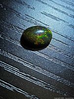 Oval cabochon black opal placed on textured surface showing multicolour fire