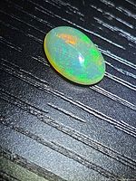 Oval crystal opal showing green and orange play-of-color on dark background