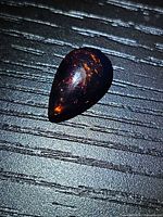 Pear-shaped black opal showing dark body tone with red fire