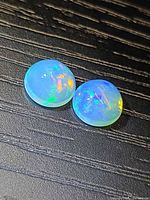 Pair of round cabochon opals displaying play-of-colour on dark surface