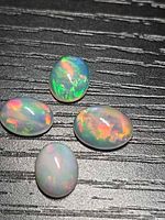 Four oval cabochon opals on black textured background showing play of color