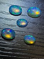 Five oval jelly opal cabochons showing play-of-color on dark surface