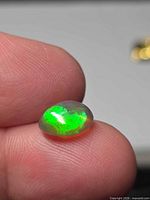 Opal showing bright green play-of-color on fingertip