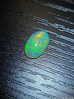 Top view of oval crystal opal showing bright green, orange pinfire play-of-colour