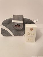 Miniature perfume box in front of grey denim Dior cosmetic bag