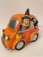 Front left view of orange Halloween car figurine with witch driver and pumpkins
