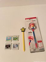 Overview of four 3DS cartridges, yellow star stylus, sealed Mario bobblehead stylus