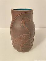 Full view of brown stoneware vase with carved heron scene and teal interior