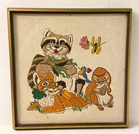 Full view of framed needlepoint showing raccoon, fox, squirrel, bird, butterfly