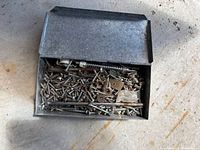 Rectangular galvanized box open showing assorted screws, anchors and small hardware