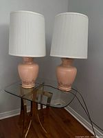 Both peach ceramic table lamps with shades on glass table