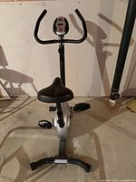 Front view of upright exercise bike showing console, seat, pedals and base.