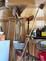 Group of long-handled garden tools and hand tools hanging on wall