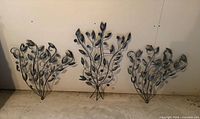 Front view of three matching metal botanical wall art pieces against wall